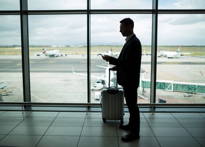 Businessman with luggage using mobile phone at airport